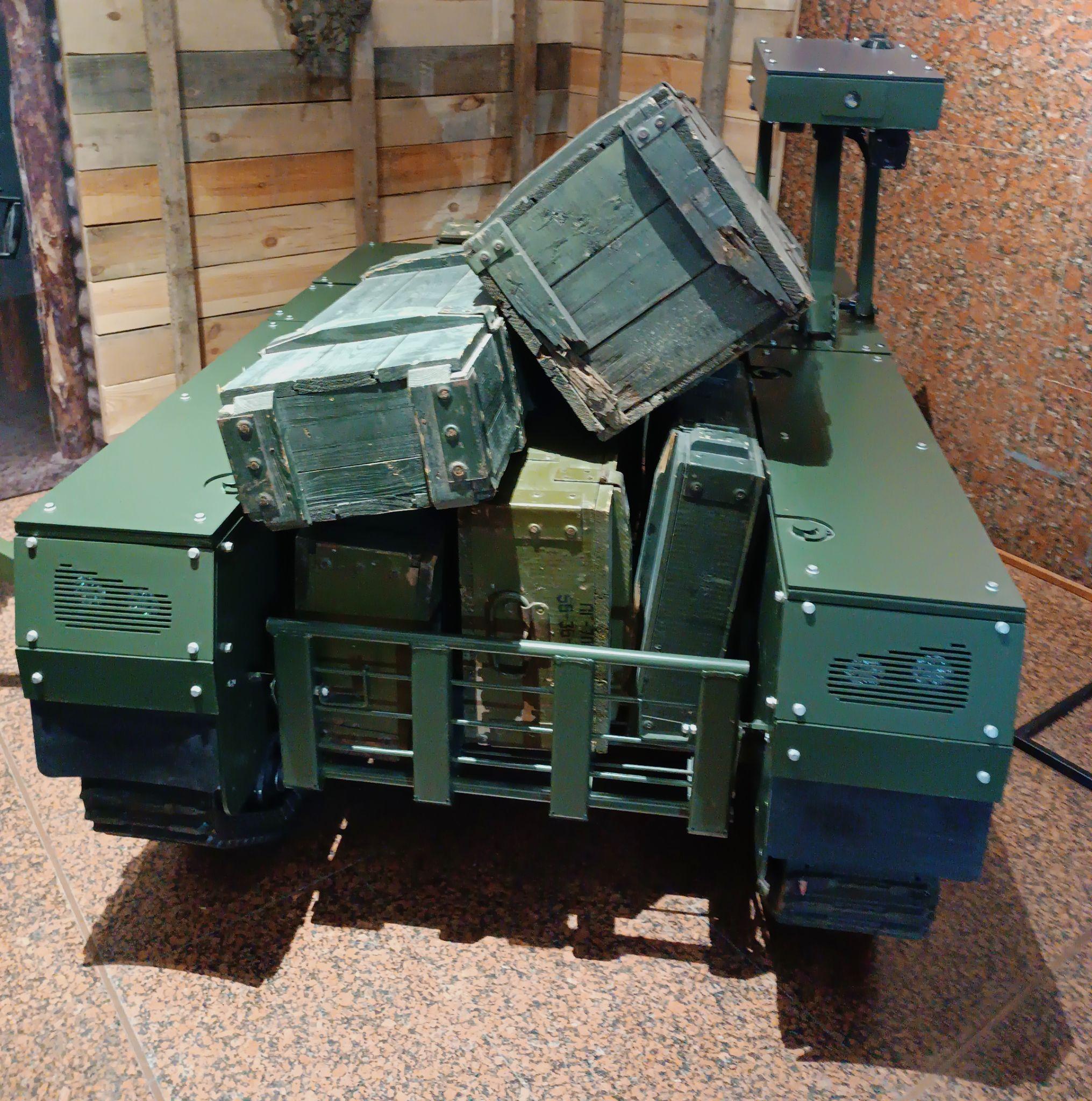 A green tracked ground robot loaded with wooden and metal ammunition boxes.