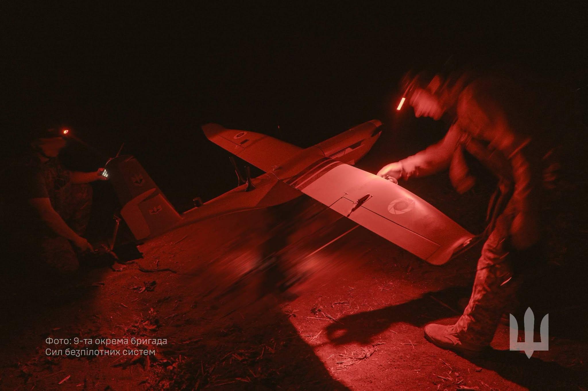 At night, in the red light of head torches, two service members prepare a fixed-wing strike drone for take-off.